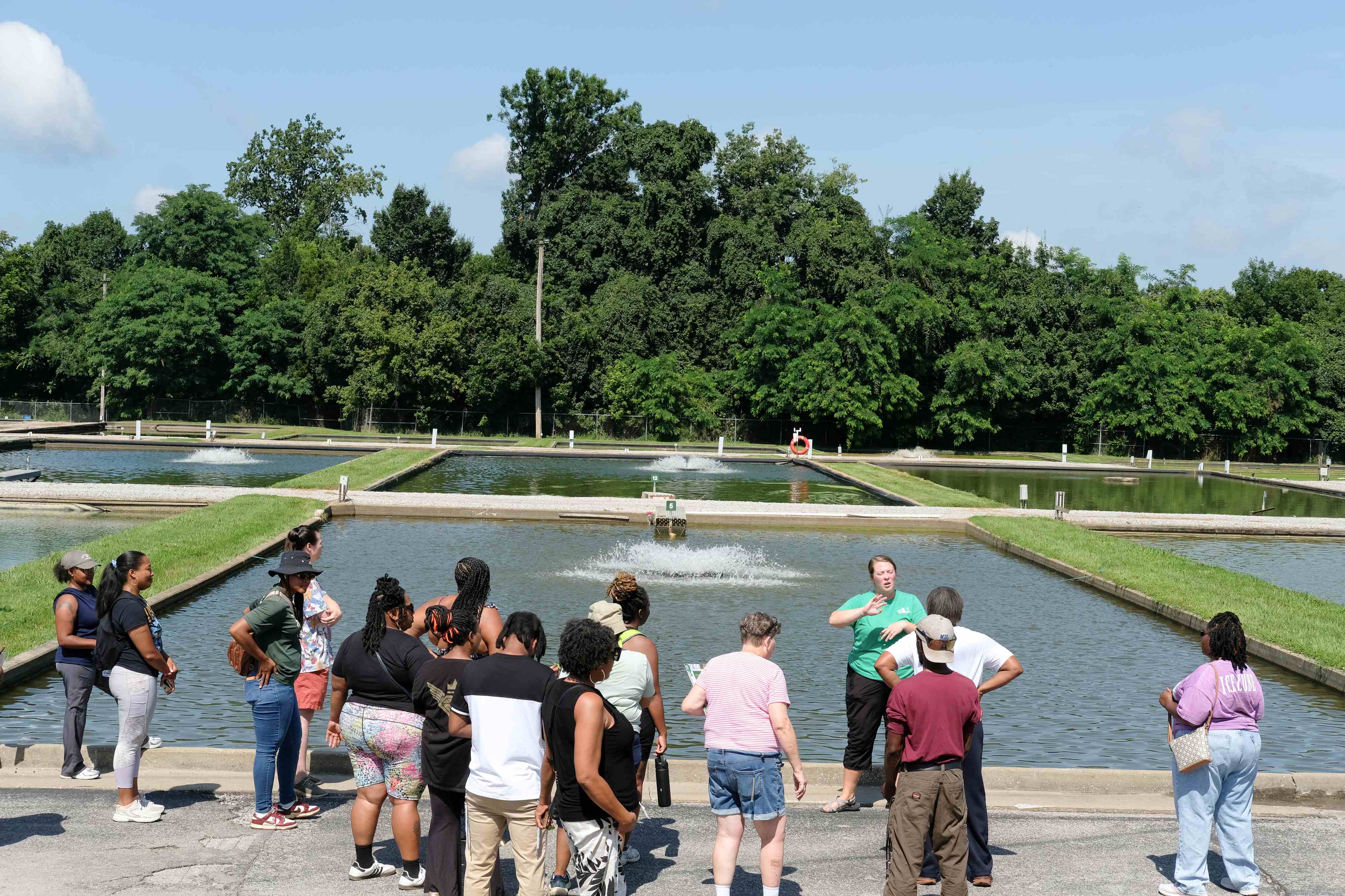 Participants gathered around KSU staff while she speaks to the group in front of outdoor Aquaculture facilities.