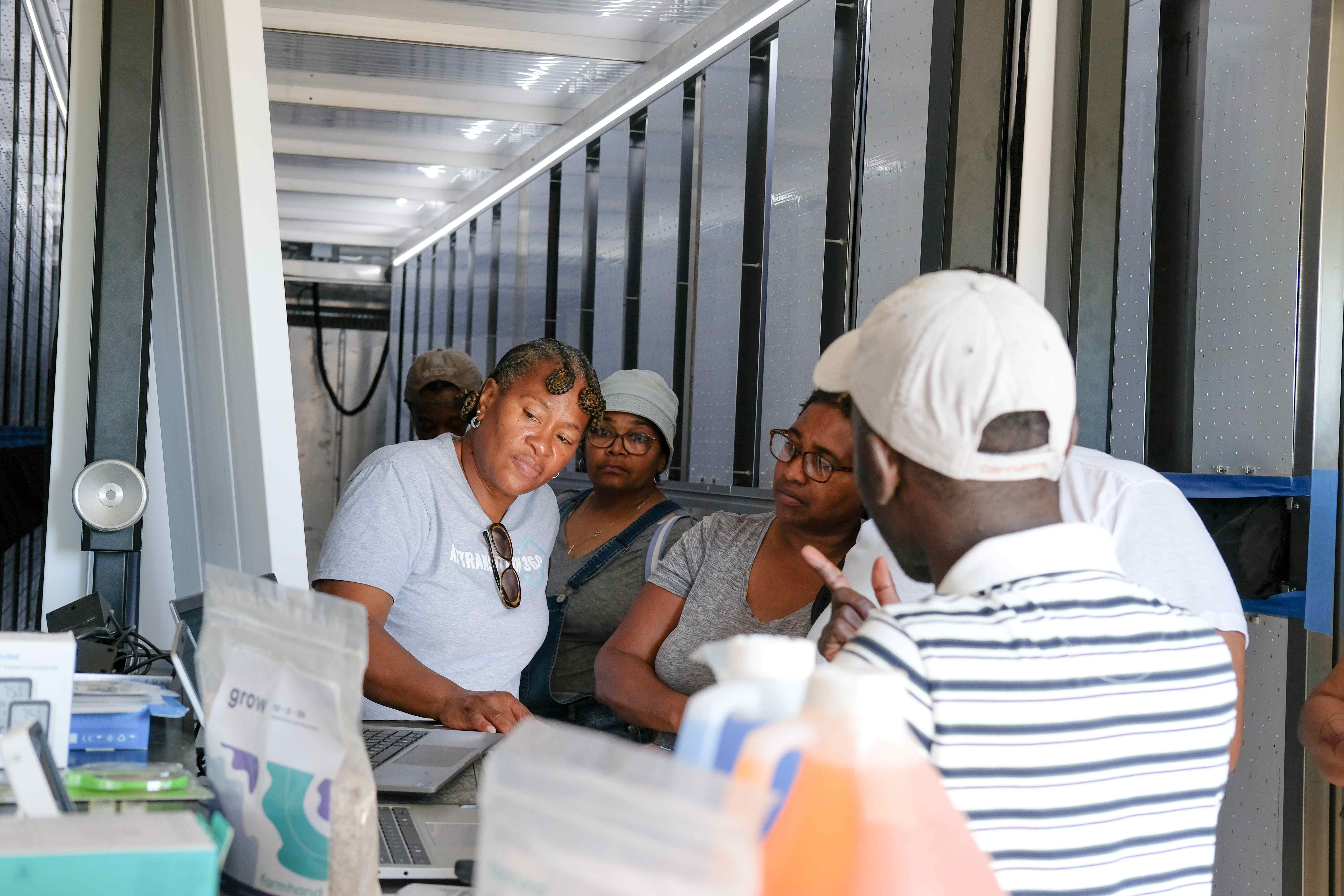 Participants listening to Arnold Katende speak inside a shipping container hydroponics system.